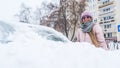 Happy young caucasian woman in pink jacked cleaning irst snow from her car