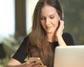 Happy young cheerful woman smiling, sitting in the office, working from home, using laptop computer and mobile phone Royalty Free Stock Photo