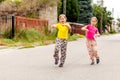 Happy young children on the town street, two joyful cheerful little school age girls jumping, walking on the street together Royalty Free Stock Photo