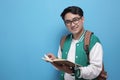 Male Asian student smiling and reading a book against blue background Royalty Free Stock Photo
