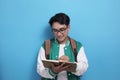 Young Asian male student wearing green baseball jacket writing on book Royalty Free Stock Photo