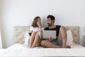 Happy young couple on bed online shopping. Happy smiling young couple in love at home, sitting on bed looking at laptop computer Royalty Free Stock Photo