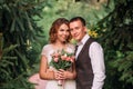 Happy young couple, a blond bride in light white amazing wedding dress, holding bouquet of pink flowers, and groom