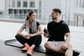 Happy young couple brunette beautiful woman and handsome man in sportswear having rest on yoga mat, drinking water after Royalty Free Stock Photo