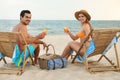 Happy young couple with cocktails sitting on deck chairs at beach Royalty Free Stock Photo