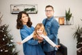 Happy young couple with daughter celebrating Christmas together at home near Christmas tree. Man and woman hold flying girl. Royalty Free Stock Photo