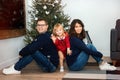 Happy young couple with daughter celebrating Christmas together at home near Christmas tree. Man and woman sitting and girl Royalty Free Stock Photo