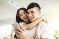 Happy young couple embracing while looking at mobile phone in living room at home Royalty Free Stock Photo