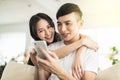Happy young couple embracing while looking at mobile phone in living room at home Royalty Free Stock Photo