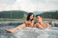 Happy young couple enjoying a bath in Jacuzzi while drinking cocktail outdoors on romantic vacation Royalty Free Stock Photo