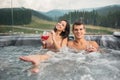 Happy young couple enjoying a bath in Jacuzzi while drinking cocktail outdoors on romantic vacation Royalty Free Stock Photo