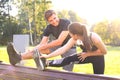 Happy young couple exercising together in a park, stretching exercises