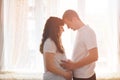 Happy young couple expecting baby standing together in front of window holding a belly and thinking of a baby Royalty Free Stock Photo