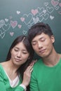 Happy young couple with eyes closed in front of blackboard with hearts