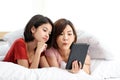 Happy young couple friend beautiful asia women lying on the bed in a bedroom and using digital tablet Royalty Free Stock Photo