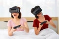 Happy young couple friend beautiful asia women playing video games virtual reality glasses on the bed in a bedroom,Gaming concept Royalty Free Stock Photo