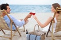 Happy young couple with glasses of wine sitting on deck chairs at beach Royalty Free Stock Photo