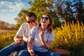 Young couple hanging in their phones and laughing outside. Woman and man relaing after having picnic at sunset.