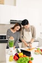 Happy young couple have fun in modern kitchen indoor while preparing fresh fruits and vegetables food salad