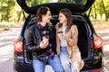 Happy young couple having a coffee break during road trip in countryside. Man and woman sitting in car trunk and having coffee Royalty Free Stock Photo