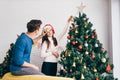 Happy young couple having fun decorating various baubles on the Christmas tree in the living room at home. Royalty Free Stock Photo