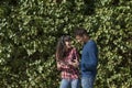 Happy young couple having fun over green ivy background. The woman is listening to music on mobile phone and headset and the man Royalty Free Stock Photo