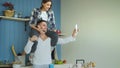 Happy young couple having fun and talking online video call in the kitchen at home. Girl is sitting on boyfriend`s neck Royalty Free Stock Photo