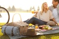 Happy young couple having picnic near lake, focus on basket with blanket and hat Royalty Free Stock Photo