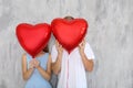 Happy young couple hiding faces behind heart shaped red balloons near grey wall Royalty Free Stock Photo
