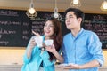 Happy couple holding cup of coffee in cafÃÂ©. Cheerful young woman pointing fingers to boyfriend see something in outdoor