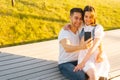 Happy young couple hugging and sharing media in smartphone sitting relaxed on bench in city park on bench in summer Royalty Free Stock Photo