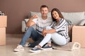 Happy young couple with key from their new house and moving boxes sitting on floor indoors Royalty Free Stock Photo