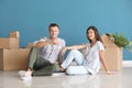 Happy young couple with key from their new house and moving boxes sitting on floor indoors Royalty Free Stock Photo