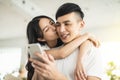 Happy young couple kissing and  looking at mobile phone in living room at home Royalty Free Stock Photo