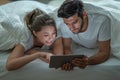 Happy young couple looking a tablet together and laughing while lying on the bed at night Royalty Free Stock Photo