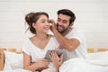 Happy young couple looking a tablet together and laughing while lying on the bed Royalty Free Stock Photo