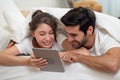 Happy young couple looking a tablet together and laughing while lying on the bed Royalty Free Stock Photo