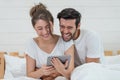 Happy young couple looking a tablet together and laughing while lying on the bed Royalty Free Stock Photo