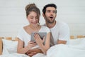 Happy young couple looking a tablet together and laughing while lying on the bed Royalty Free Stock Photo