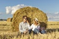 Happy young couple in love sitting in field near hay bale. Royalty Free Stock Photo