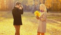 Happy young couple, man photographs woman with film camera and yellow maple leaves in autumn park on warm sunny day Royalty Free Stock Photo