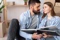 happy young couple on moving day sitting on floor in casual clothes hugging looking at photo album, family tradition to Royalty Free Stock Photo