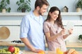 Happy young couple in pajamas watching online content in a didital tablet and smiling in kitchen at home Royalty Free Stock Photo