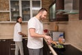 Happy young couple preparing breakfast, man fries broccoli, scrambled eggs. Girl slices fresh vegetables. On self-isolation during