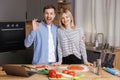 Happy young couple is preparing healthy and tasty food on modern kitchen. Attractive woman and man looking at camera, the man Royalty Free Stock Photo