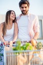 Happy young couple is pushing shopping cart filled with grocery bags Royalty Free Stock Photo