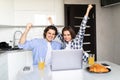 Happy young couple with raised arms of win celebrate looking on laptop in kitchen Royalty Free Stock Photo