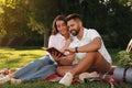 Happy young couple reading book on plaid in park. Summer picnic Royalty Free Stock Photo