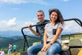 Happy young couple resting on the dirty offroad car. Highland car tour