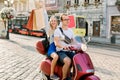 Happy young couple riding a scooter in the city on a sunny day. Handsome man in glasses rides a moped, while his Royalty Free Stock Photo